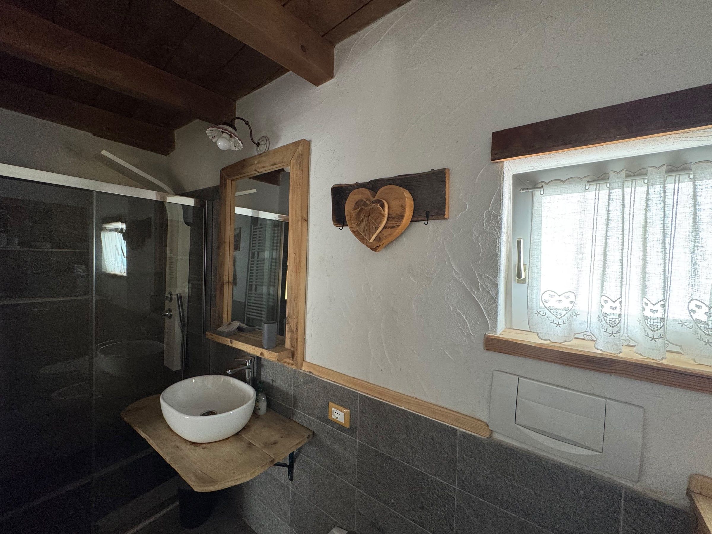 Bagno con doccia in cristallo, lavabo in appoggio su mensola in legno e specchio