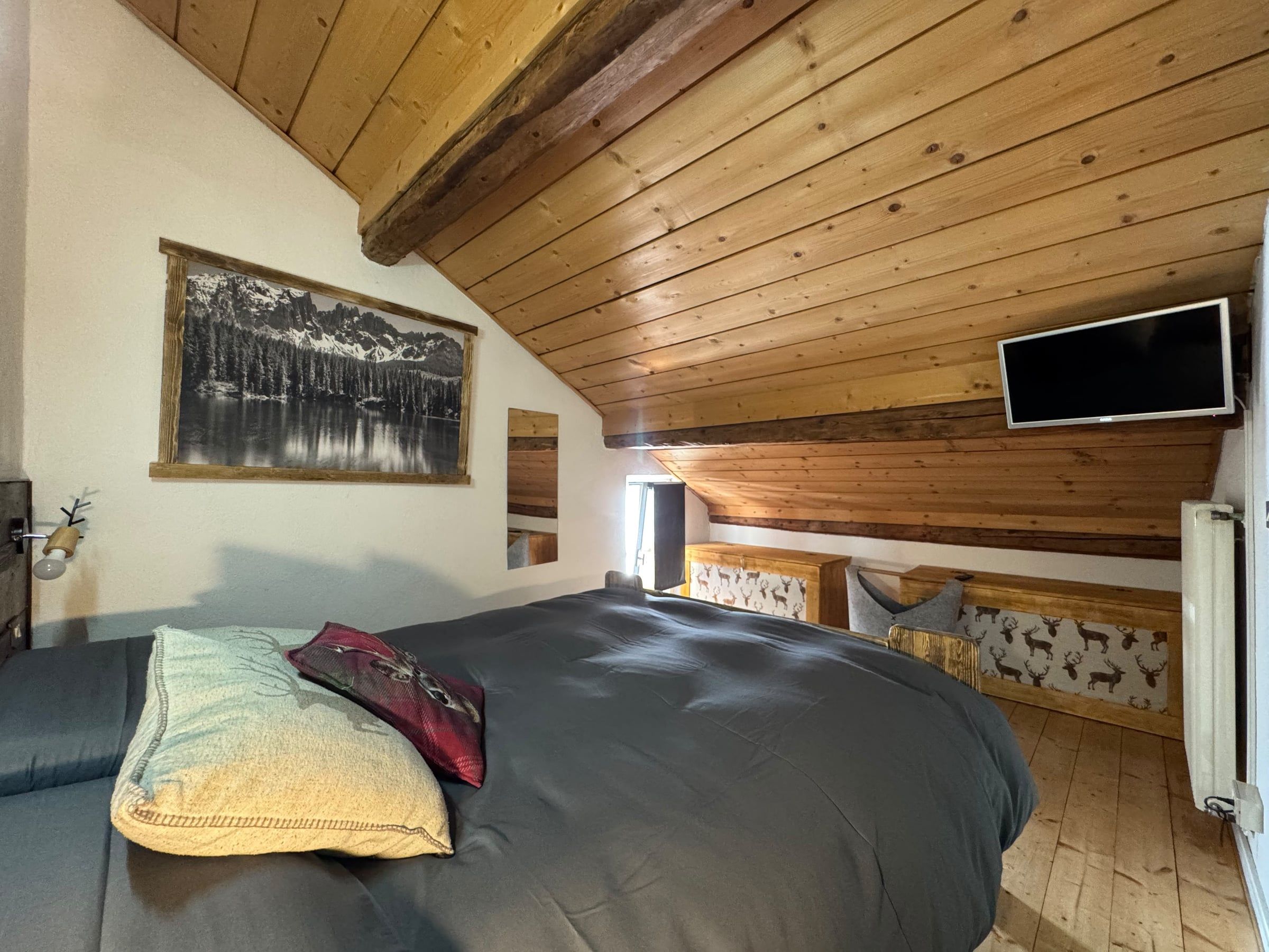 Letto matrimoniale sotto il soffitto in legno, con Smart TV e panche decorate